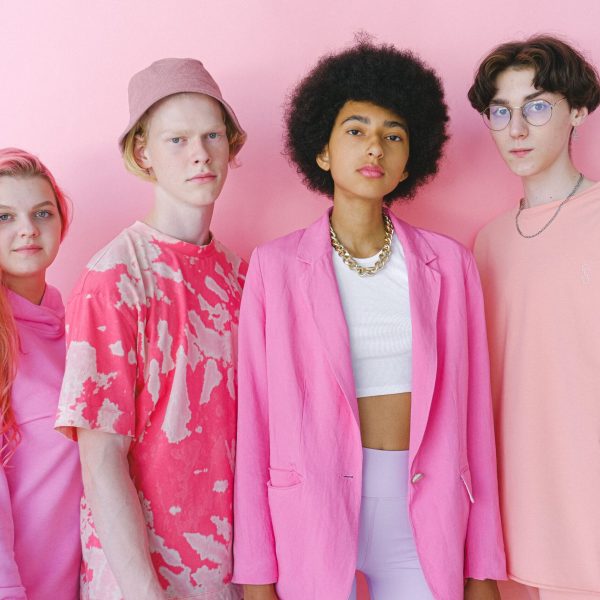 Diverse teenage friends in trendy outfits looking at camera on pink background of studio